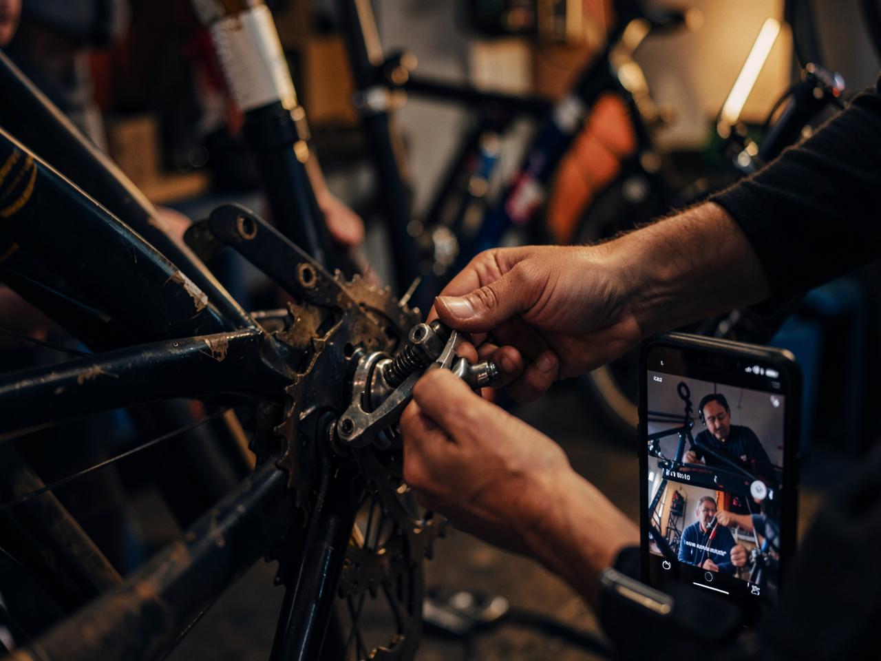 A learner repairing a bicycle while a Master guides them over a live video call
